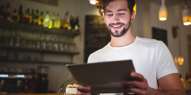 "Homem sorrindo enquanto utiliza um tablet em um restaurante, representando o uso de tecnologia, gamificação e super apps no food service."